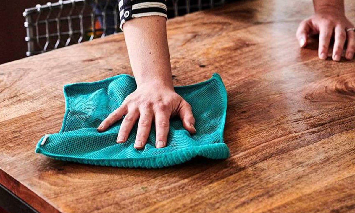 دستمال آبی در دستان زن در حال تمیز کردن میز چوبی - از بین بردن لکه آب روی چوب