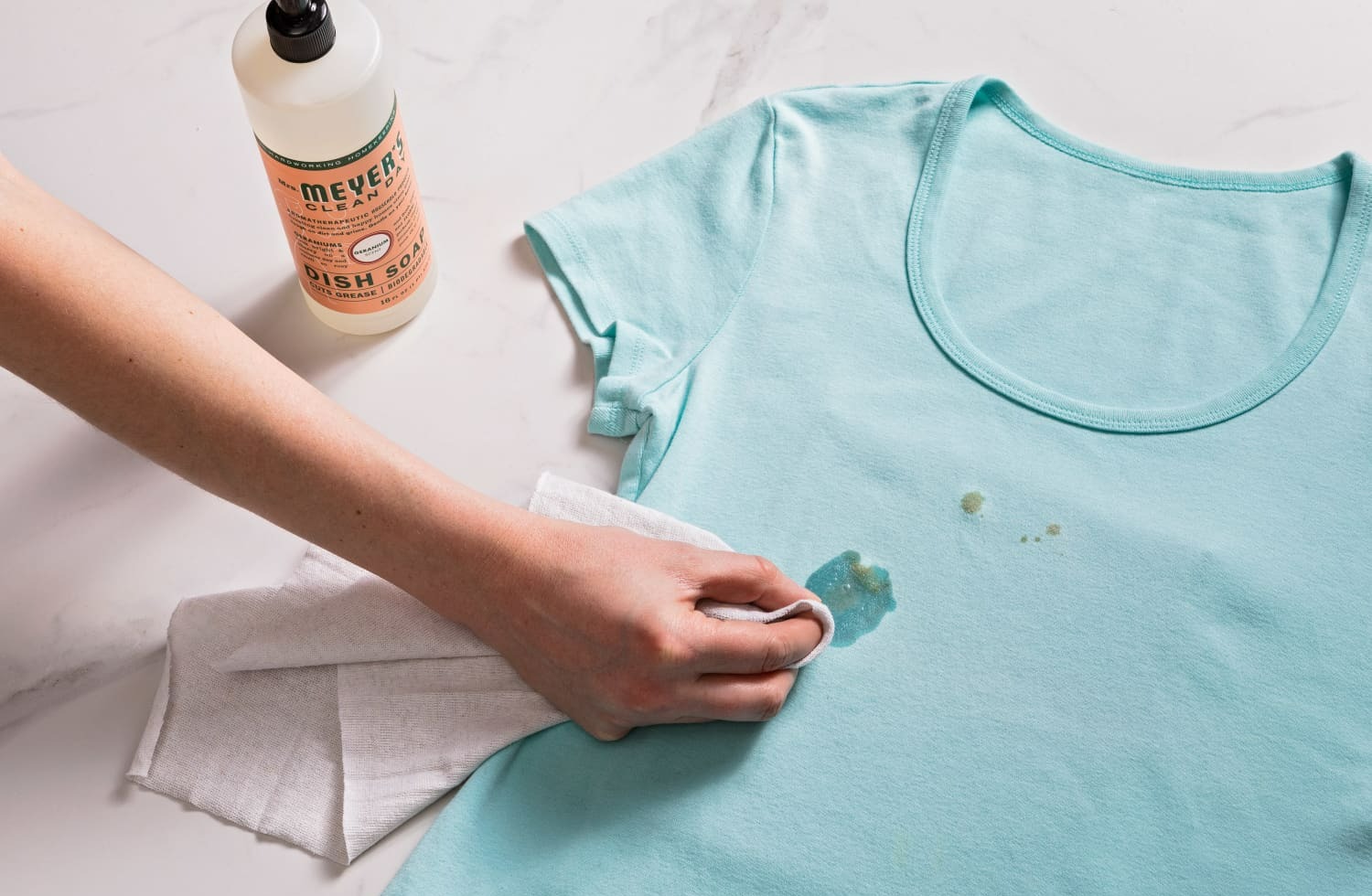 زنی در حال لکه گیری یک تیشرت سبزابی - پاک کردن لکه مام روی لباس