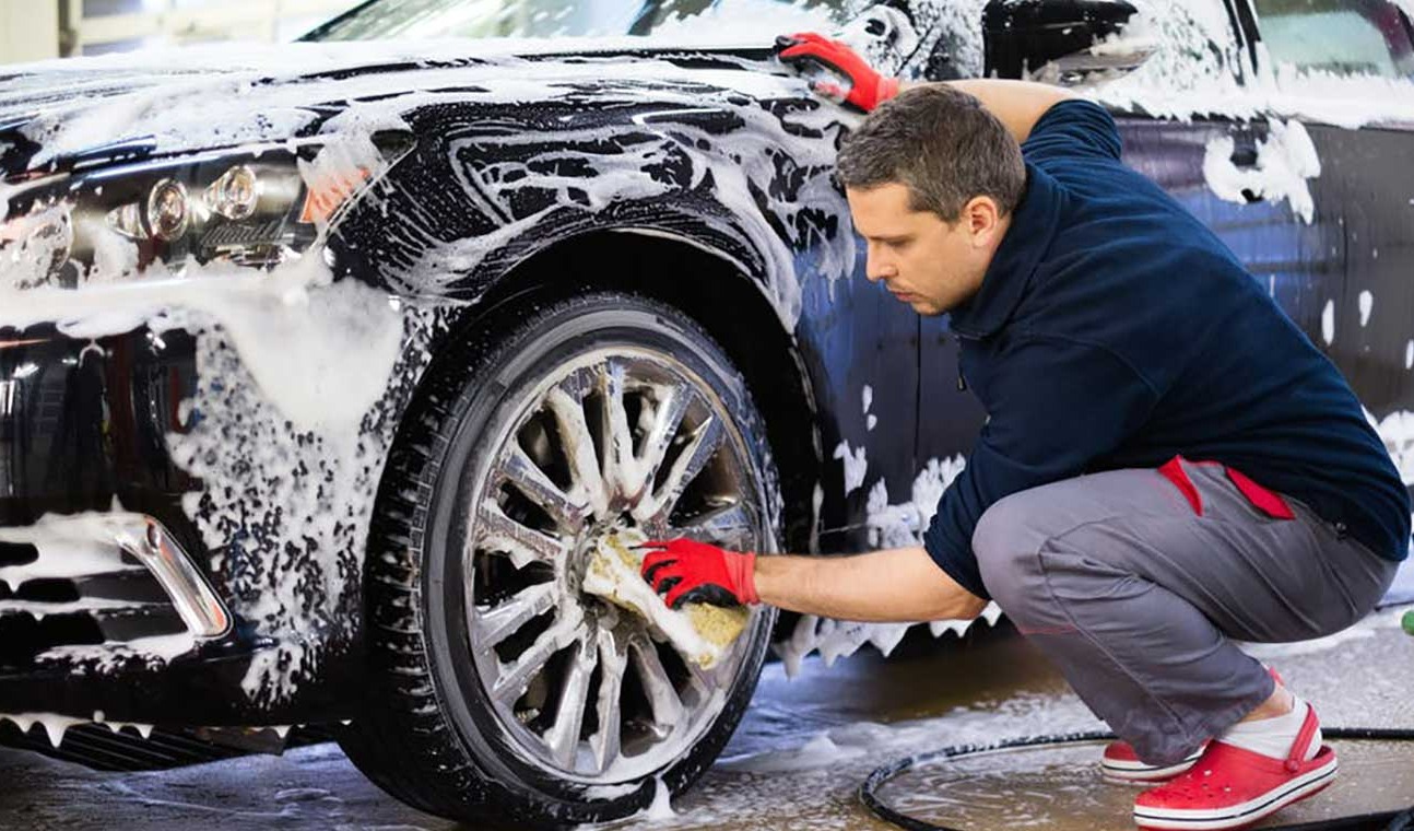 مرد در حال کفی کردن ماشین مشکی و شستن لاستیک و رینگ - شستن ماشین بدون آب