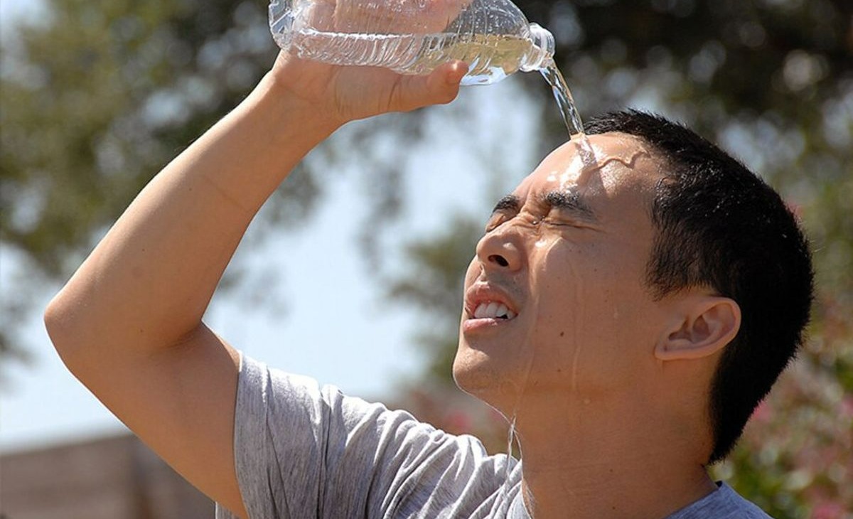 یک مرد که آب معدنی را روی صورتش خالی می کند - خنک کردن خانه بدون کولر
