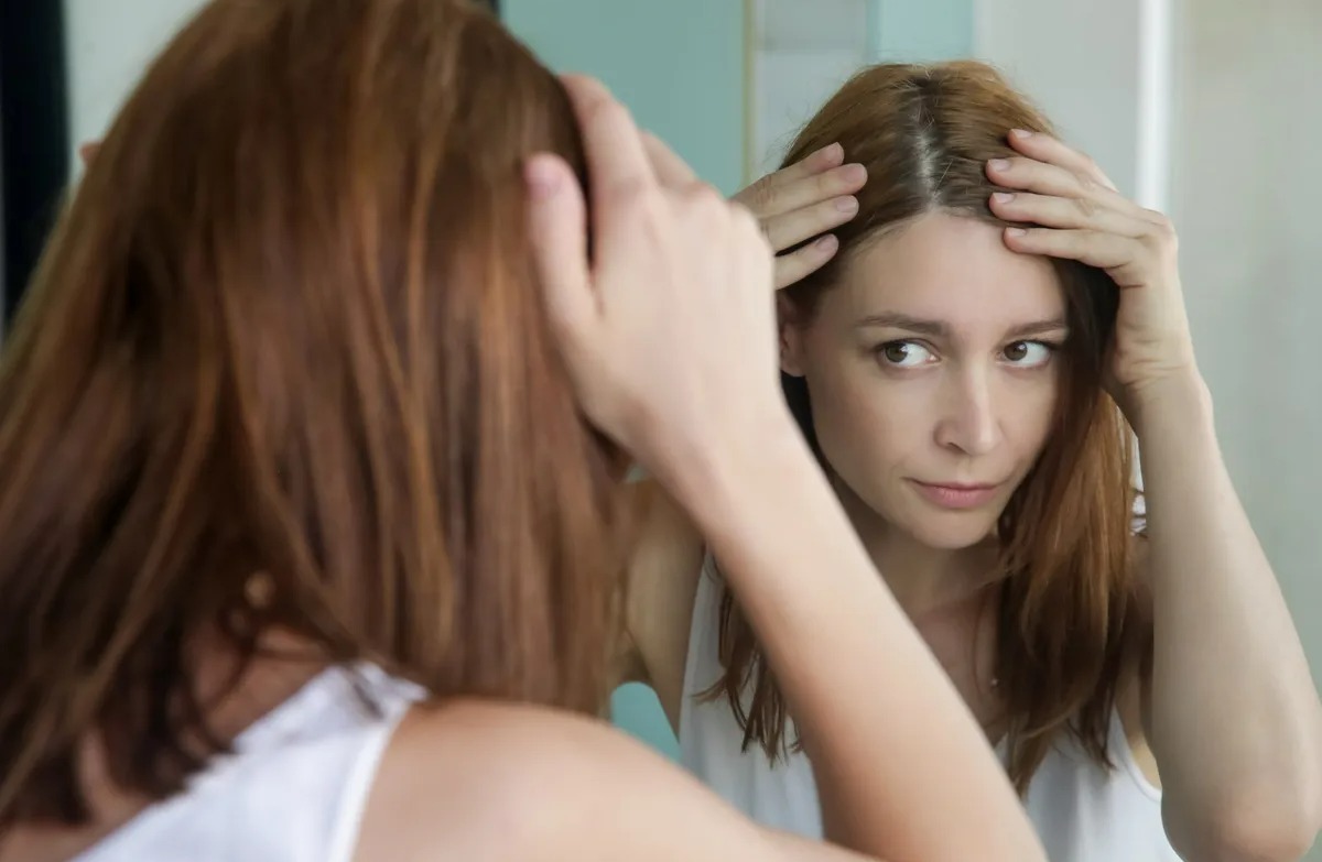 زن در حال نگاه کردن به مو در اینه - درمان خانگی ریزش مو