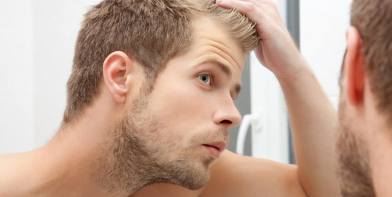 مرد در حال نگاه کردن موهایش در آینه - درمان خانگی ریزش مو