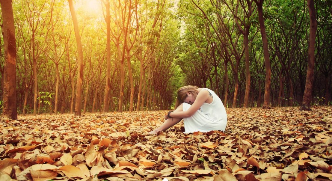 زن تنها نشسته وی برگ های پاییزی - درمان افسردگی فصلی
