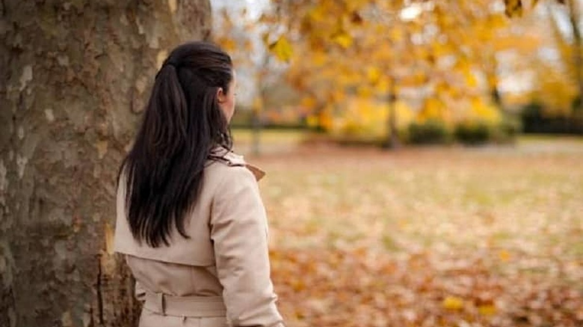 زن در حال نگاه کردن به برگ های پاییزی - درمان افسردگی فصلی