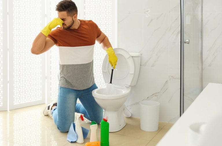 Young man feeling disgust while cleaning toilet bowl in bathroom